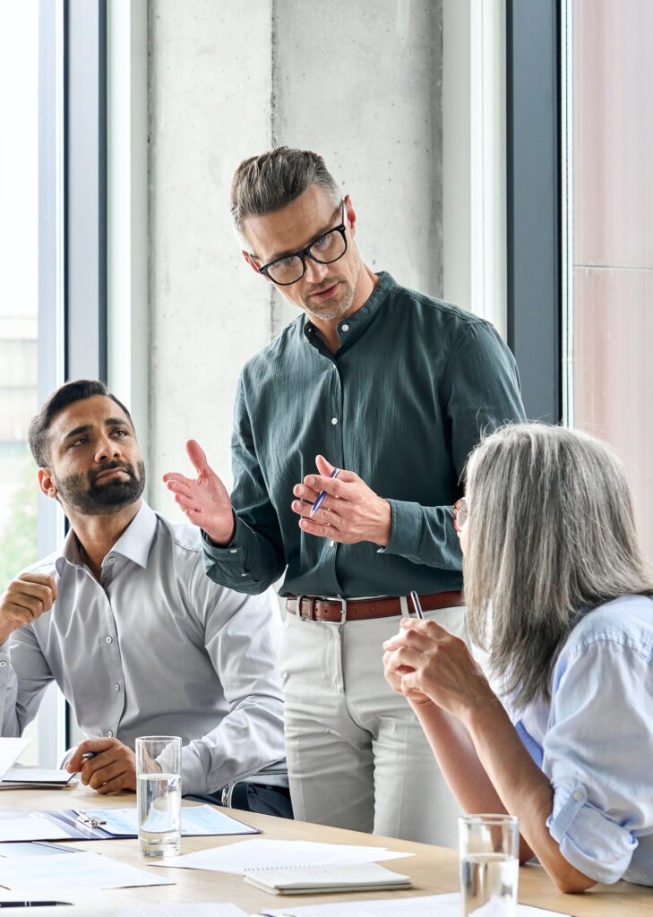 Mature businessman mentor leader talking with managers at meeting in board room.